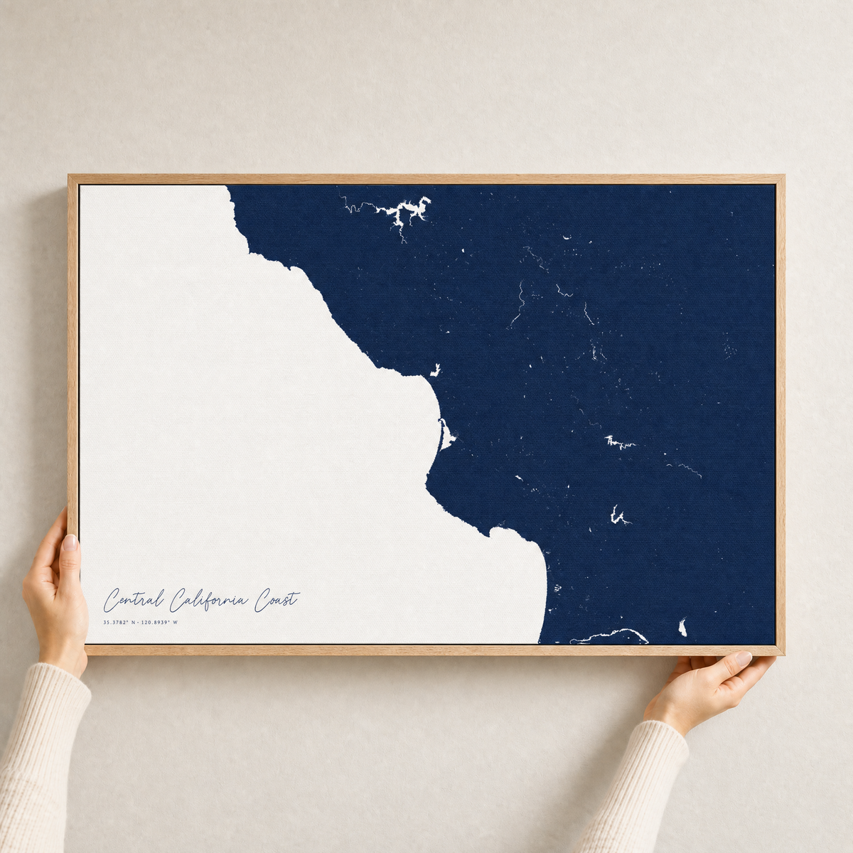 Central California Coast canvas map — hands holding the canvas in an oak frame