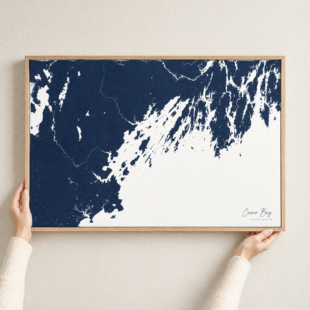 Casco Bay horizontal canvas map in Navy, hands holding an oak-framed canvas