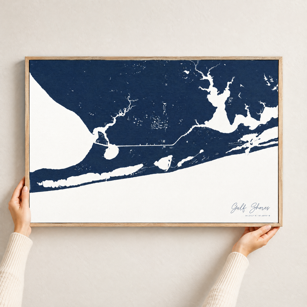 Gulf Shores horizontal canvas map in Navy, hands holding an oak-framed canvas