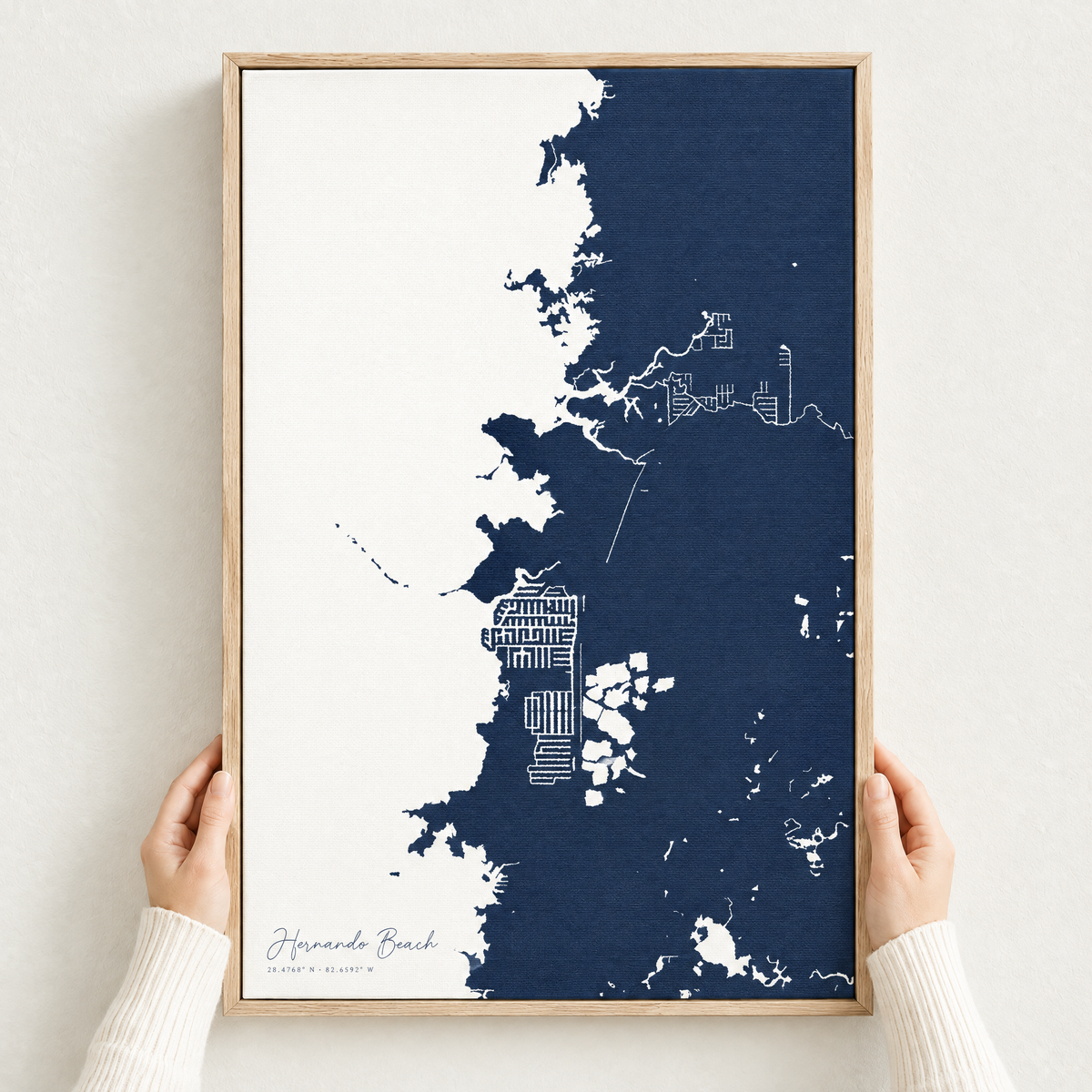 Hernando Beach vertical canvas map in Navy, hands holding an oak-framed canvas