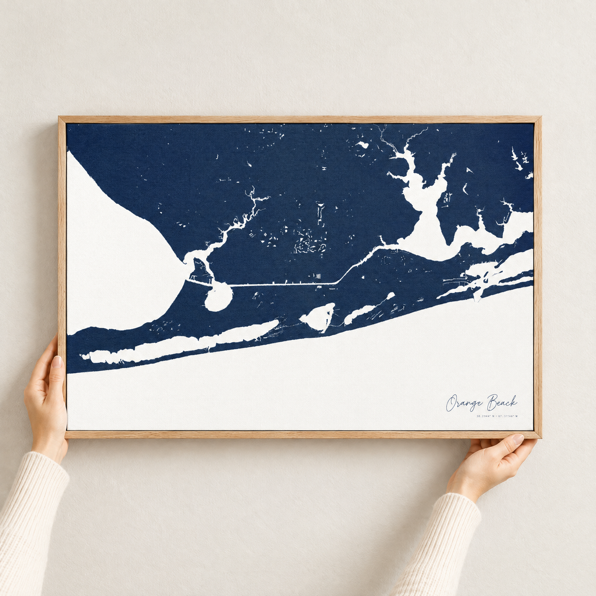 Orange Beach horizontal canvas map in Navy, hands holding an oak-framed canvas