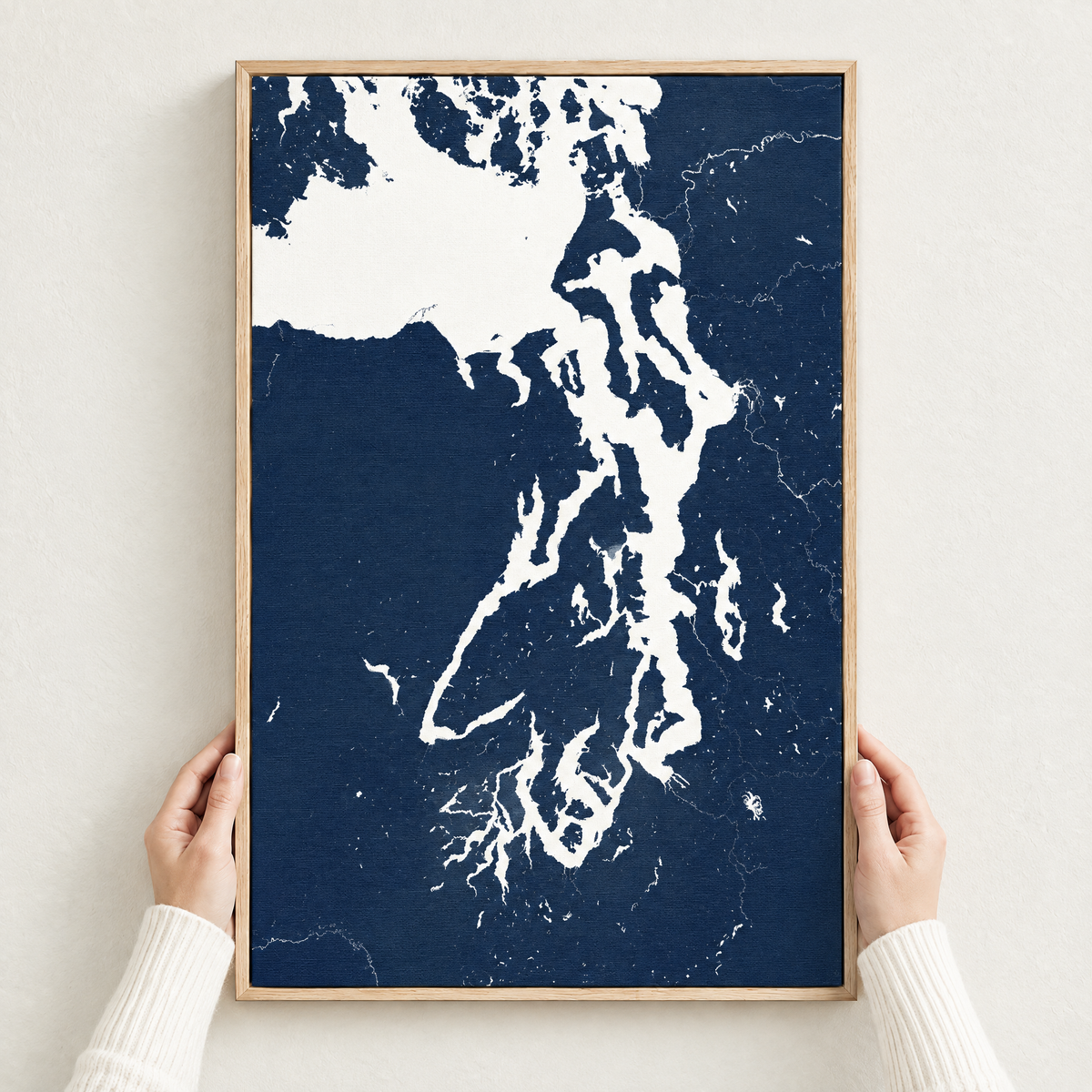 Puget Sound vertical canvas map in Navy, hands holding an oak-framed canvas