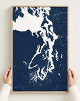 Puget Sound vertical canvas map in Navy, hands holding an oak-framed canvas