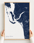 Southwest Florida canvas map — hands holding the canvas in an oak frame