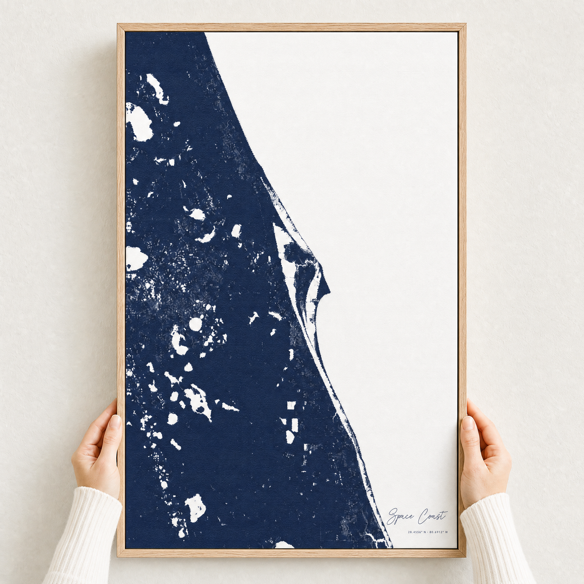Space Coast canvas map — hands holding the canvas in an oak frame