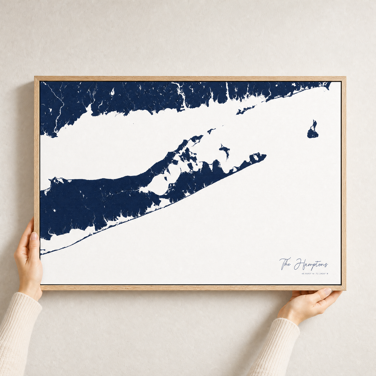The Hamptons canvas map — hands holding the canvas in an oak frame