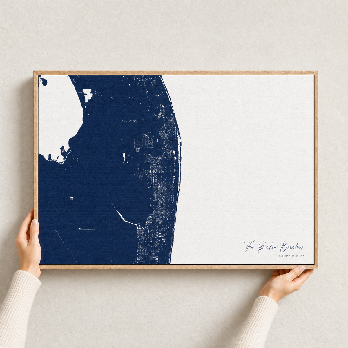 The Palm Beaches canvas map — hands holding the canvas in an oak frame